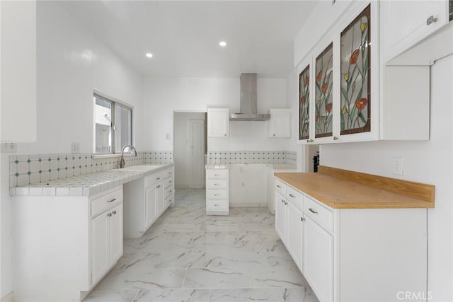 kitchen featuring sink, wall chimney range hood, white cabinets, and decorative backsplash