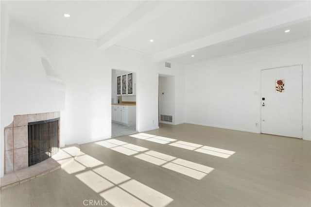 unfurnished living room with a tile fireplace, beam ceiling, and light hardwood / wood-style floors