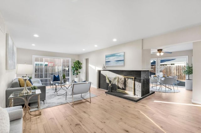 living room featuring a multi sided fireplace, ceiling fan, and light wood-type flooring