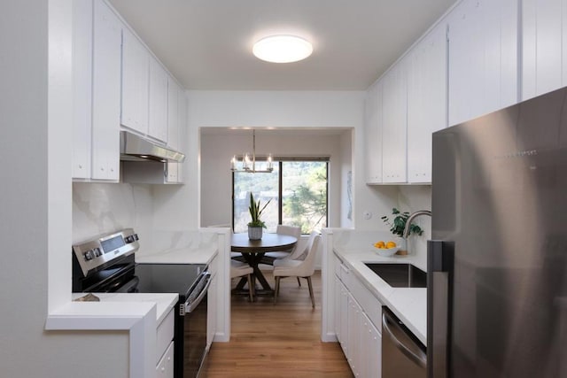 kitchen with appliances with stainless steel finishes, white cabinetry, sink, hanging light fixtures, and light hardwood / wood-style flooring