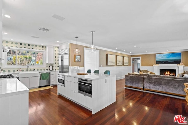 kitchen with white cabinetry, built in appliances, decorative light fixtures, and a kitchen island