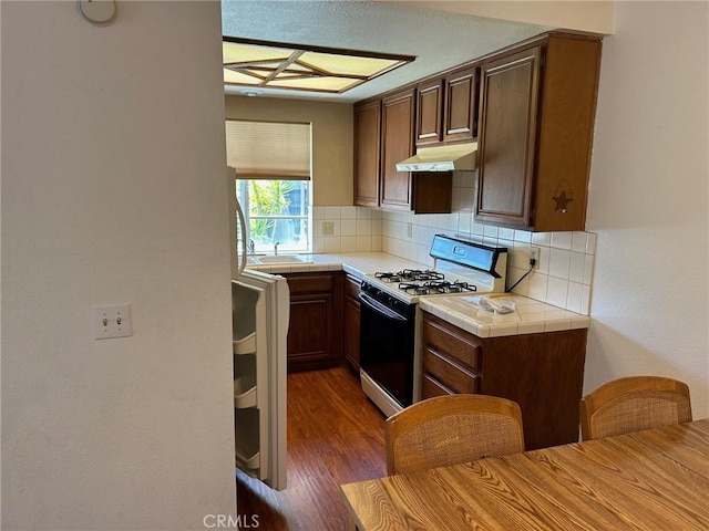 kitchen with tasteful backsplash, tile countertops, range with gas stovetop, and dark hardwood / wood-style floors