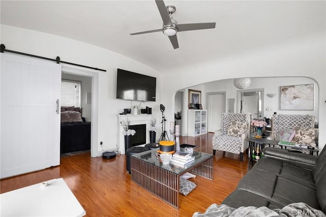 living room featuring hardwood / wood-style flooring, ceiling fan, a barn door, and vaulted ceiling