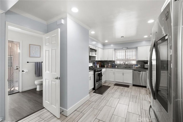 kitchen with appliances with stainless steel finishes, tasteful backsplash, sink, white cabinets, and crown molding