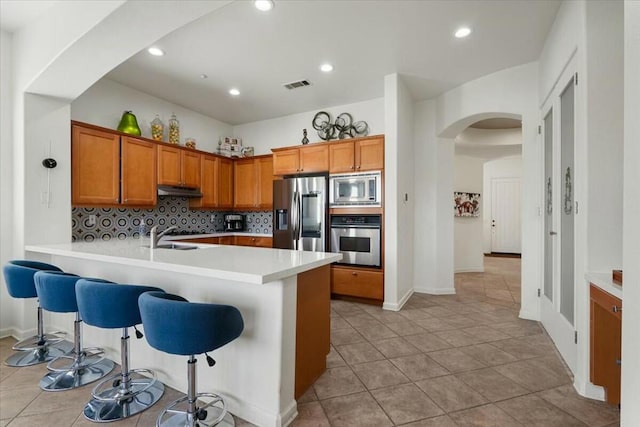 kitchen with appliances with stainless steel finishes, sink, a breakfast bar area, backsplash, and kitchen peninsula