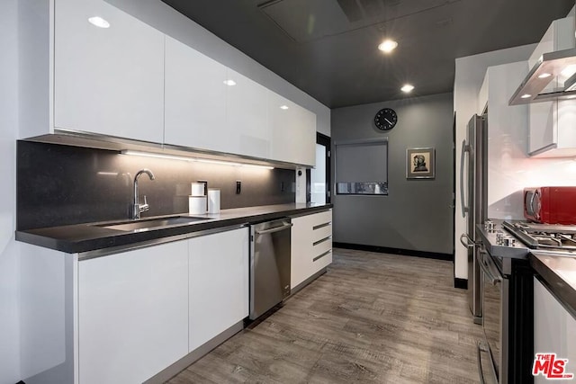 kitchen featuring sink, white cabinetry, hardwood / wood-style flooring, stainless steel appliances, and wall chimney range hood