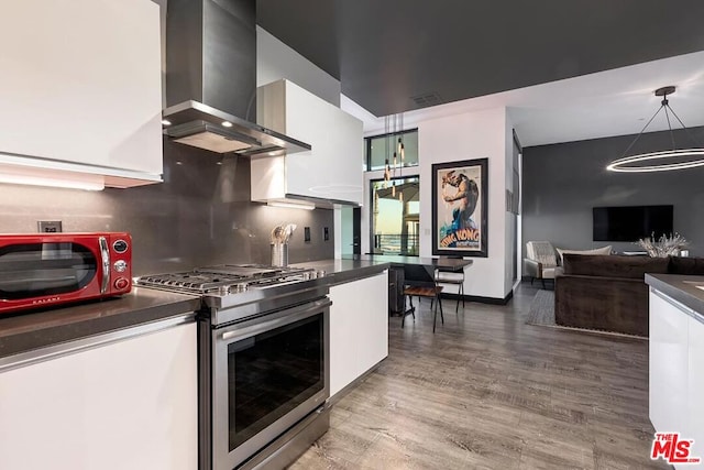 kitchen featuring wall chimney exhaust hood, stainless steel gas range, wood-type flooring, decorative light fixtures, and white cabinets