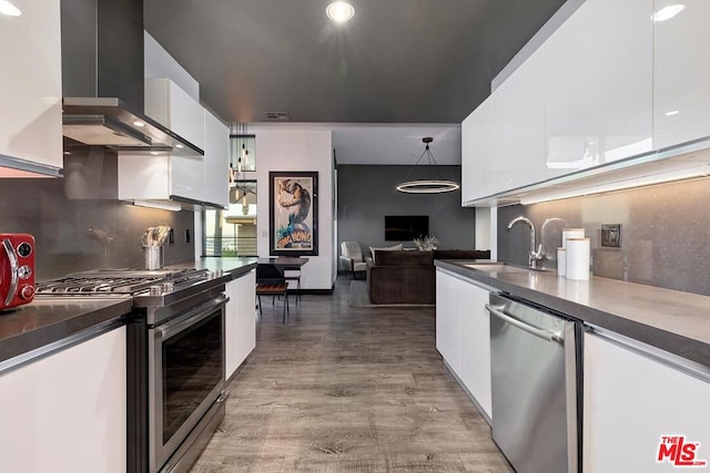 kitchen with sink, white cabinets, hardwood / wood-style flooring, stainless steel appliances, and wall chimney range hood