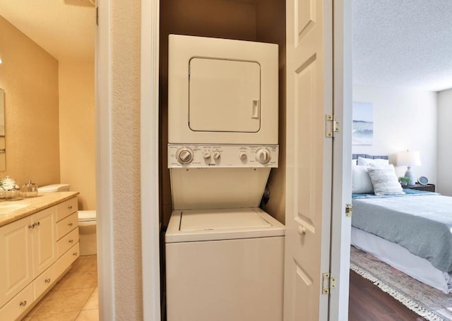 clothes washing area featuring sink, stacked washer / drying machine, light tile patterned floors, and a textured ceiling