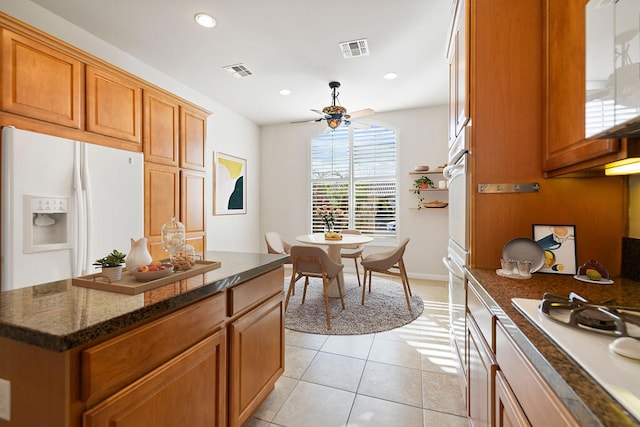 kitchen featuring white appliances, dark stone countertops, light tile patterned floors, a kitchen island, and ceiling fan