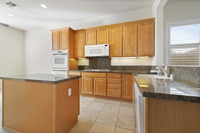 kitchen featuring light tile patterned flooring, a kitchen island, sink, dark stone counters, and white appliances