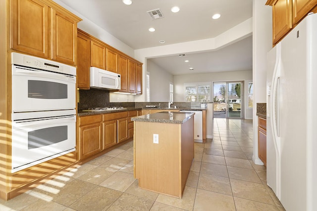 kitchen featuring light tile patterned floors, kitchen peninsula, a kitchen island, white appliances, and backsplash