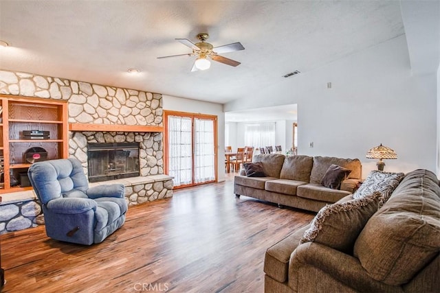 living room with lofted ceiling, hardwood / wood-style floors, a stone fireplace, and ceiling fan