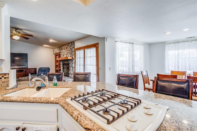 kitchen with light stone counters, white cabinetry, white gas stovetop, and sink