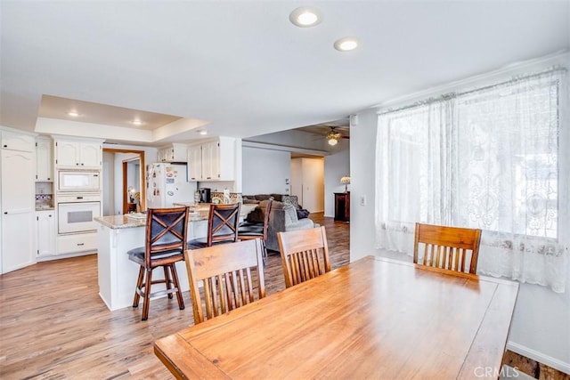 dining area featuring a raised ceiling, ceiling fan, and light hardwood / wood-style flooring