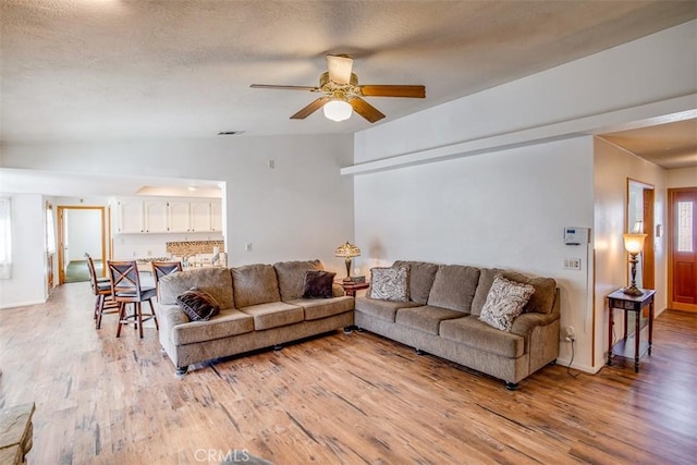 living room featuring lofted ceiling, ceiling fan, light hardwood / wood-style floors, and a textured ceiling