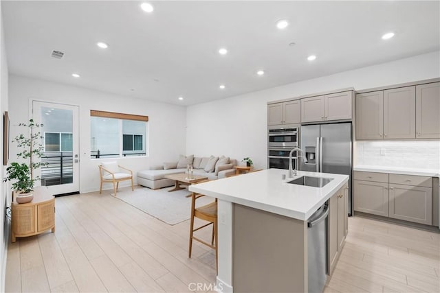 kitchen with a kitchen island with sink, decorative backsplash, gray cabinetry, and appliances with stainless steel finishes