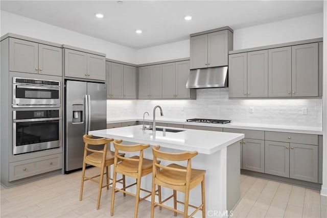 kitchen featuring gray cabinets, sink, a kitchen bar, stainless steel appliances, and a center island with sink