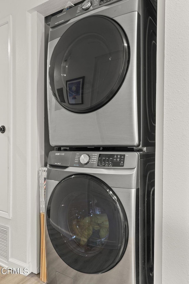 laundry room featuring hardwood / wood-style flooring and stacked washer and dryer