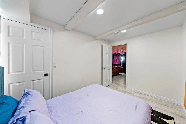 bedroom featuring a spacious closet, beam ceiling, and light wood-type flooring