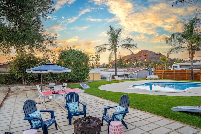 pool at dusk featuring a mountain view, a yard, a patio area, and an outdoor fire pit