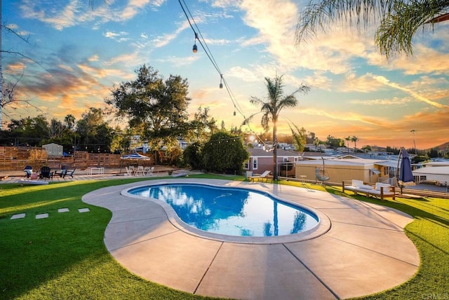 pool at dusk featuring a yard and a patio