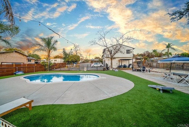 pool at dusk featuring a patio area and a lawn