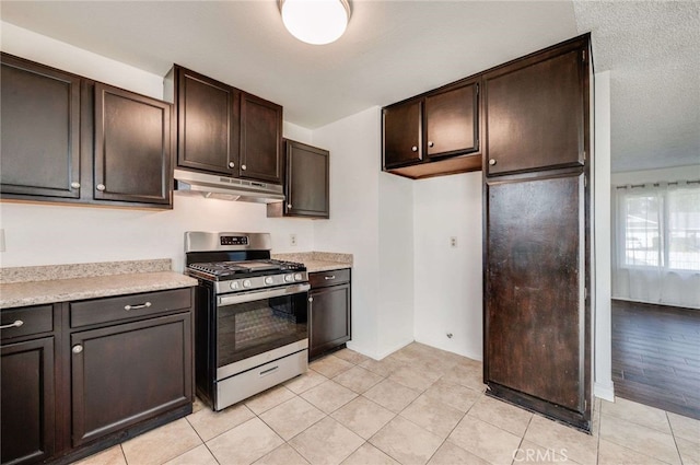 kitchen featuring light tile patterned floors, stainless steel gas range oven, under cabinet range hood, light countertops, and dark brown cabinets