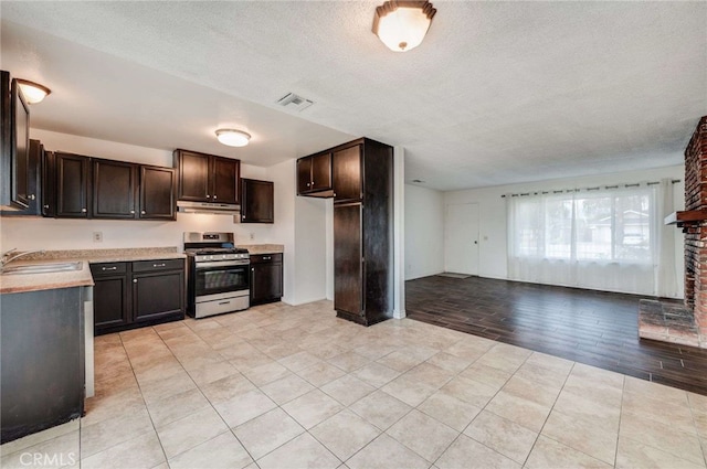 kitchen featuring stainless steel gas range oven, visible vents, light countertops, under cabinet range hood, and a sink