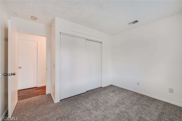 unfurnished bedroom with a closet, visible vents, carpet flooring, a textured ceiling, and baseboards