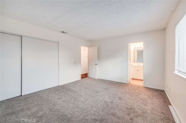 unfurnished bedroom featuring a textured ceiling, carpet floors, a closet, and connected bathroom