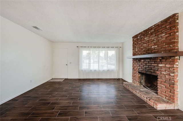 unfurnished living room featuring a brick fireplace, visible vents, a textured ceiling, and wood finish floors