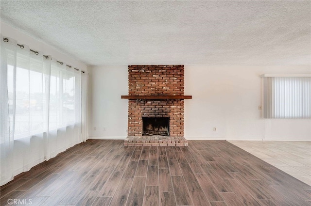 unfurnished living room featuring dark wood-style floors, a textured ceiling, a fireplace, and baseboards