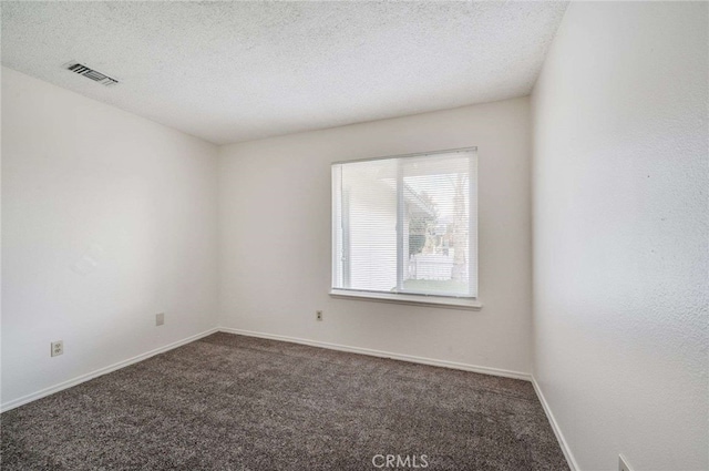 spare room with visible vents, dark carpet, a textured ceiling, and baseboards