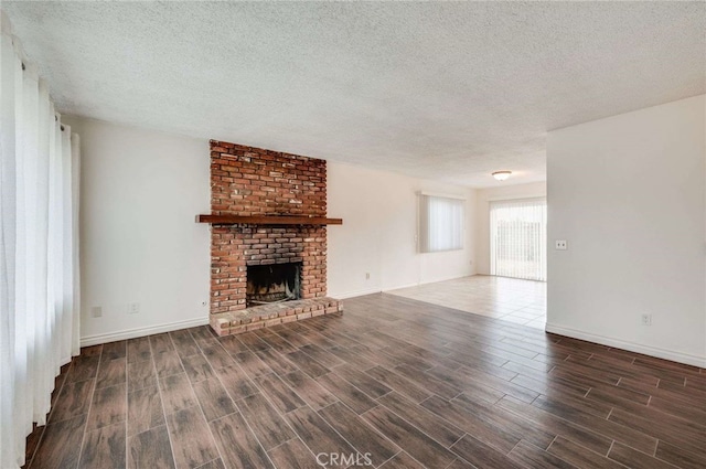 unfurnished living room with wood tiled floor, a brick fireplace, a textured ceiling, and baseboards