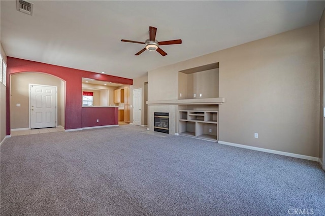 unfurnished living room featuring a tiled fireplace, light carpet, and ceiling fan