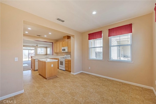 kitchen featuring light brown cabinetry, a center island, kitchen peninsula, plenty of natural light, and white appliances