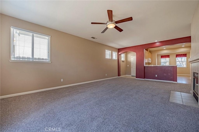 unfurnished living room with a tiled fireplace, carpet, and ceiling fan