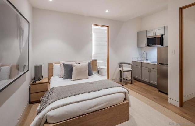 bedroom featuring connected bathroom, stainless steel fridge, and light hardwood / wood-style flooring