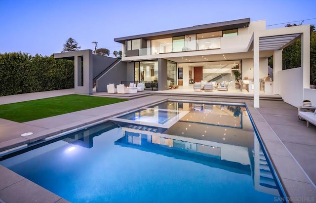 back house at dusk featuring an outdoor kitchen, a swimming pool with hot tub, outdoor lounge area, and a patio