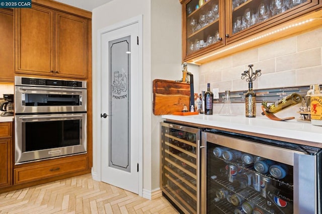 bar with tasteful backsplash, light parquet flooring, beverage cooler, and stainless steel double oven