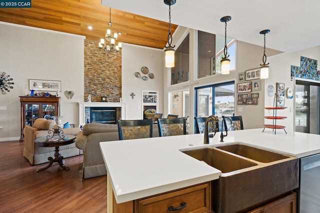 kitchen with hanging light fixtures, a stone fireplace, a kitchen island with sink, and stainless steel dishwasher