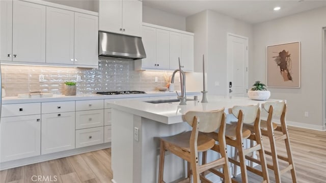 kitchen with sink, tasteful backsplash, light wood-type flooring, a kitchen island with sink, and white cabinets