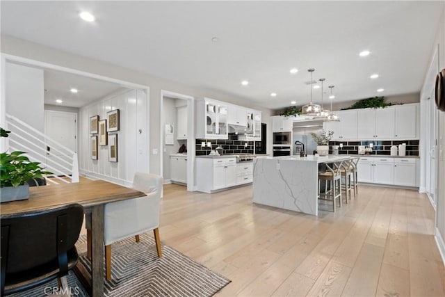 kitchen featuring tasteful backsplash, white cabinetry, a center island with sink, and light hardwood / wood-style flooring