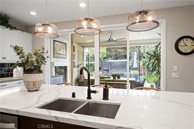 kitchen featuring ceiling fan, light stone countertops, sink, and hanging light fixtures