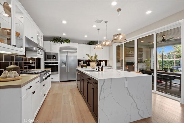 kitchen with pendant lighting, sink, built in appliances, an island with sink, and white cabinets