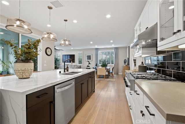 kitchen with sink, a kitchen island with sink, stainless steel appliances, white cabinets, and decorative light fixtures