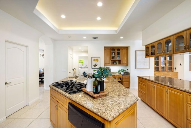 kitchen with light stone countertops, a center island, black gas cooktop, and a tray ceiling