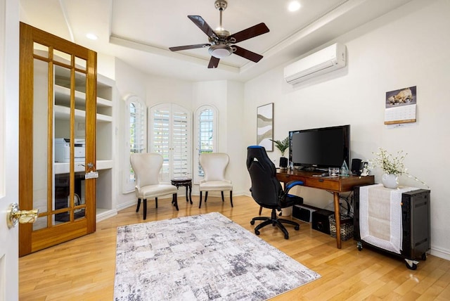 office space with ceiling fan, a wall mounted AC, light hardwood / wood-style floors, and a tray ceiling