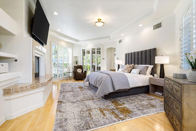 bedroom featuring a premium fireplace, access to outside, light hardwood / wood-style floors, and a tray ceiling